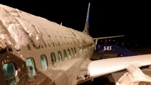 This is a common sight during travel in winter. This is a Norwegian SAS airplane on the ground and covered with snow.