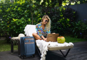 A woman sitting on a lounge chair with her laptop, next to her Travelpro bag. She's a digital nomad, able to work from wherever she can find wifi.