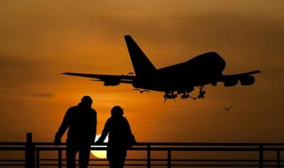 Photo of a travel couple watching the sunset as a plane flies overhead.